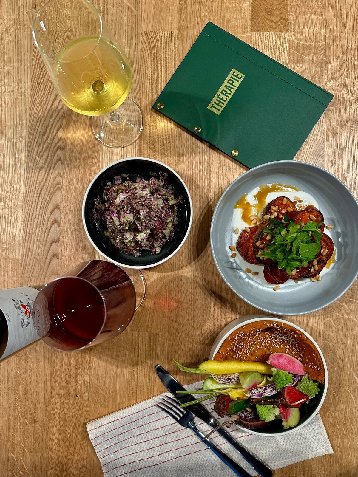 A spread of Mediterranean plates and wine on a wooden table at Therapie